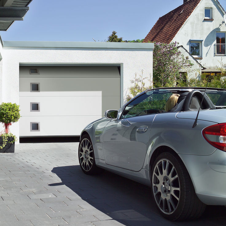 Silbernes Auto vor weißer Garage mit Sectionaltor