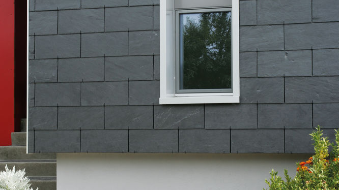 Haus mit grauer Steinfassade und weißem Fenster