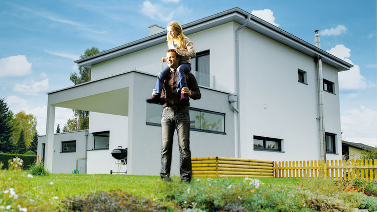 Vater mit Kind auf Wiese vor weißem Haus