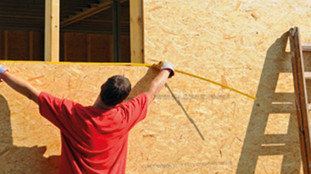 Abmessender Handwerker vor Grobspanplatten-Hauswand