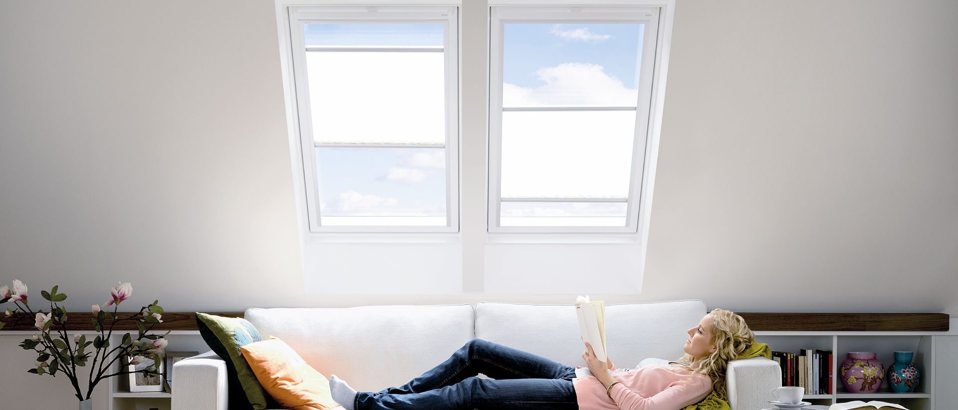 Lesende Frau auf Couch unter zwei Dachfenstern
