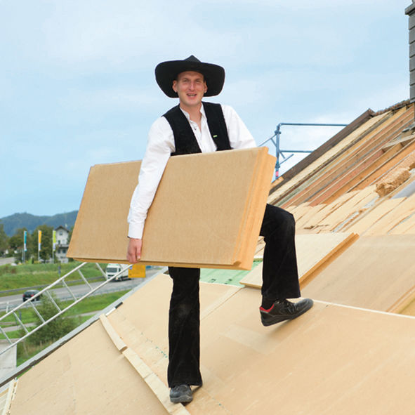 Mann mit Holzfaser-Dämmplatte am Hausdach